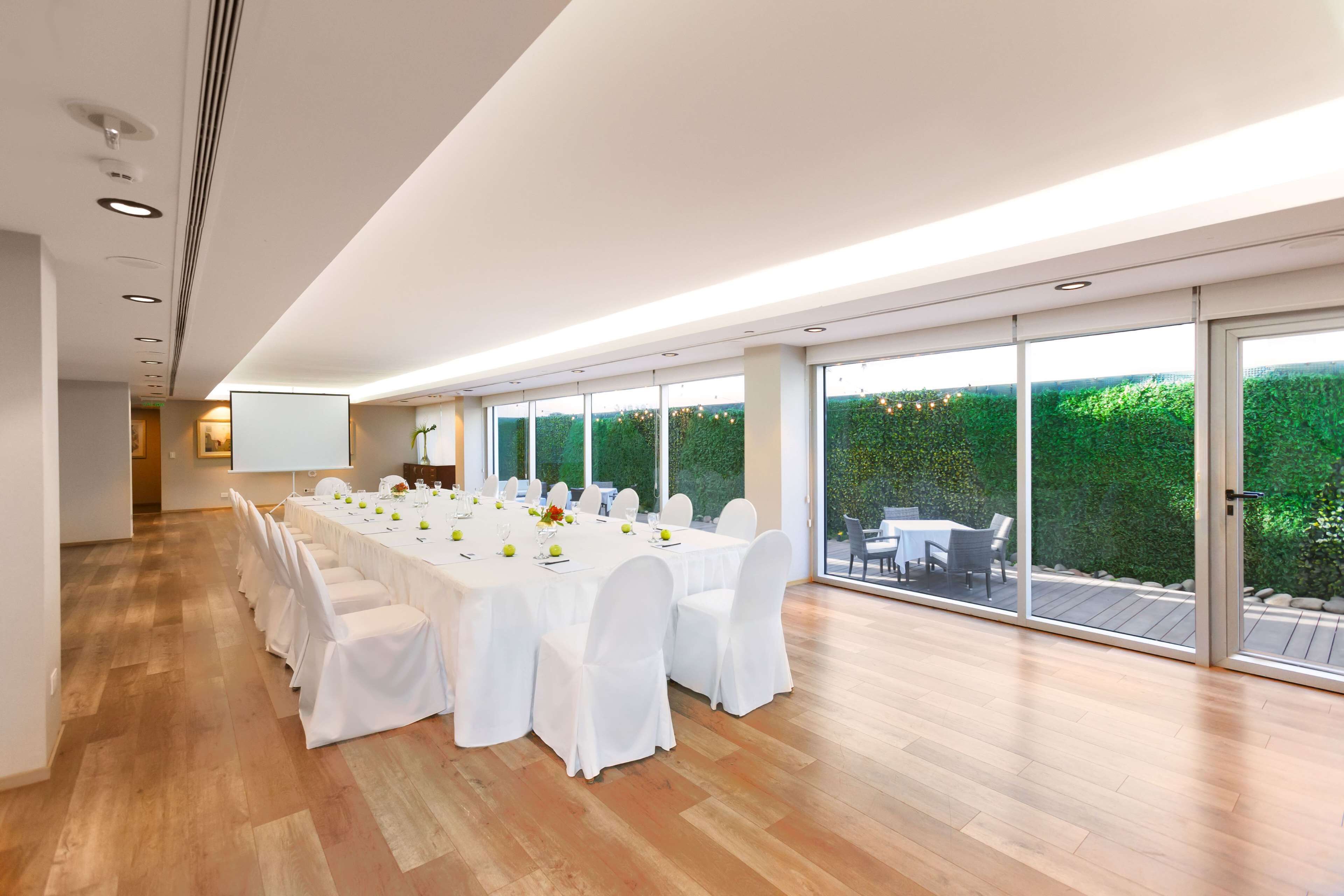 Una habitación amplia con una larga mesa dispuesta para una comida, ventanas grandes y vistas a zonas verdes al exterior.