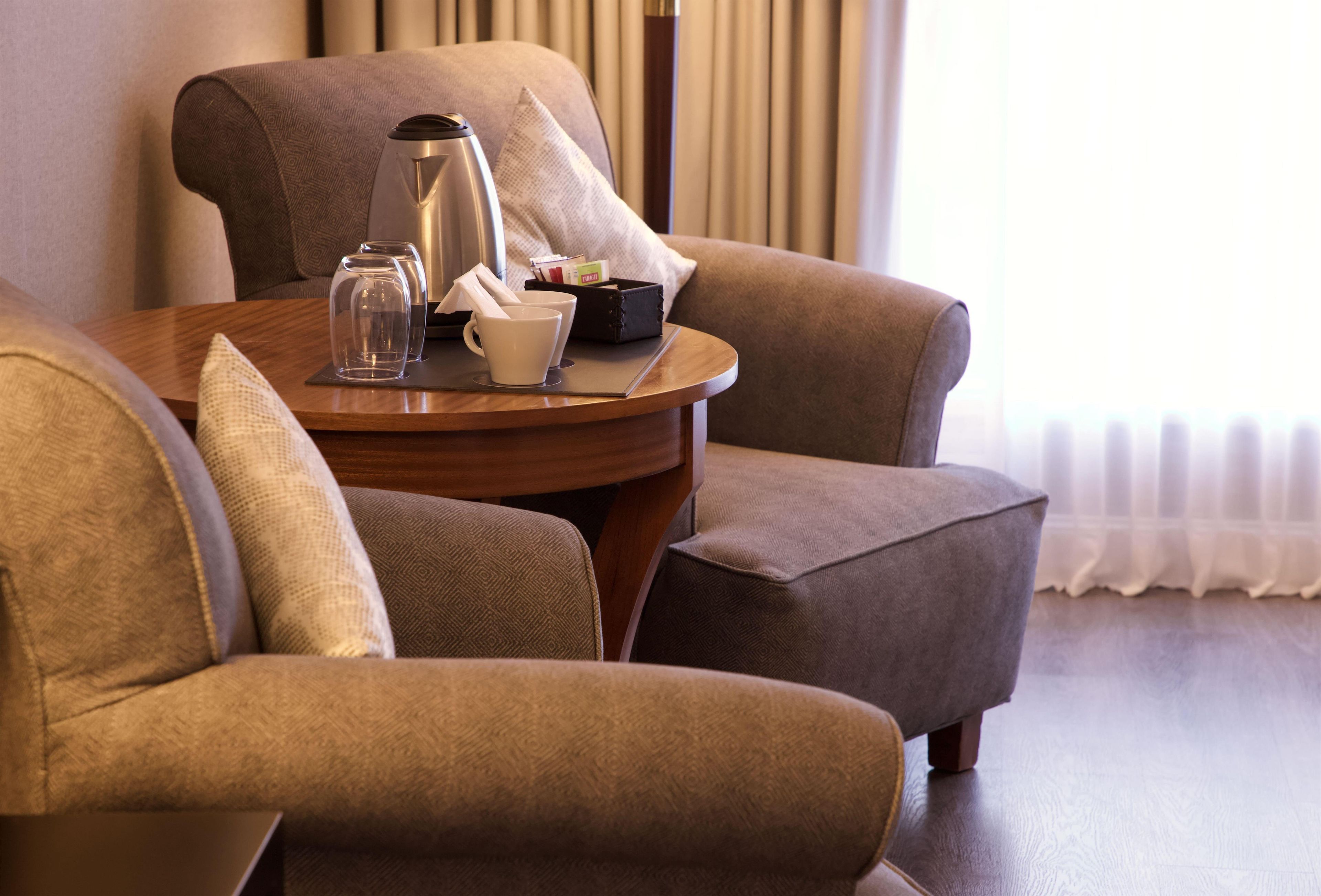 A seating area with a table, two chairs, a coffee maker, cups, and a small box, likely containing amenities.