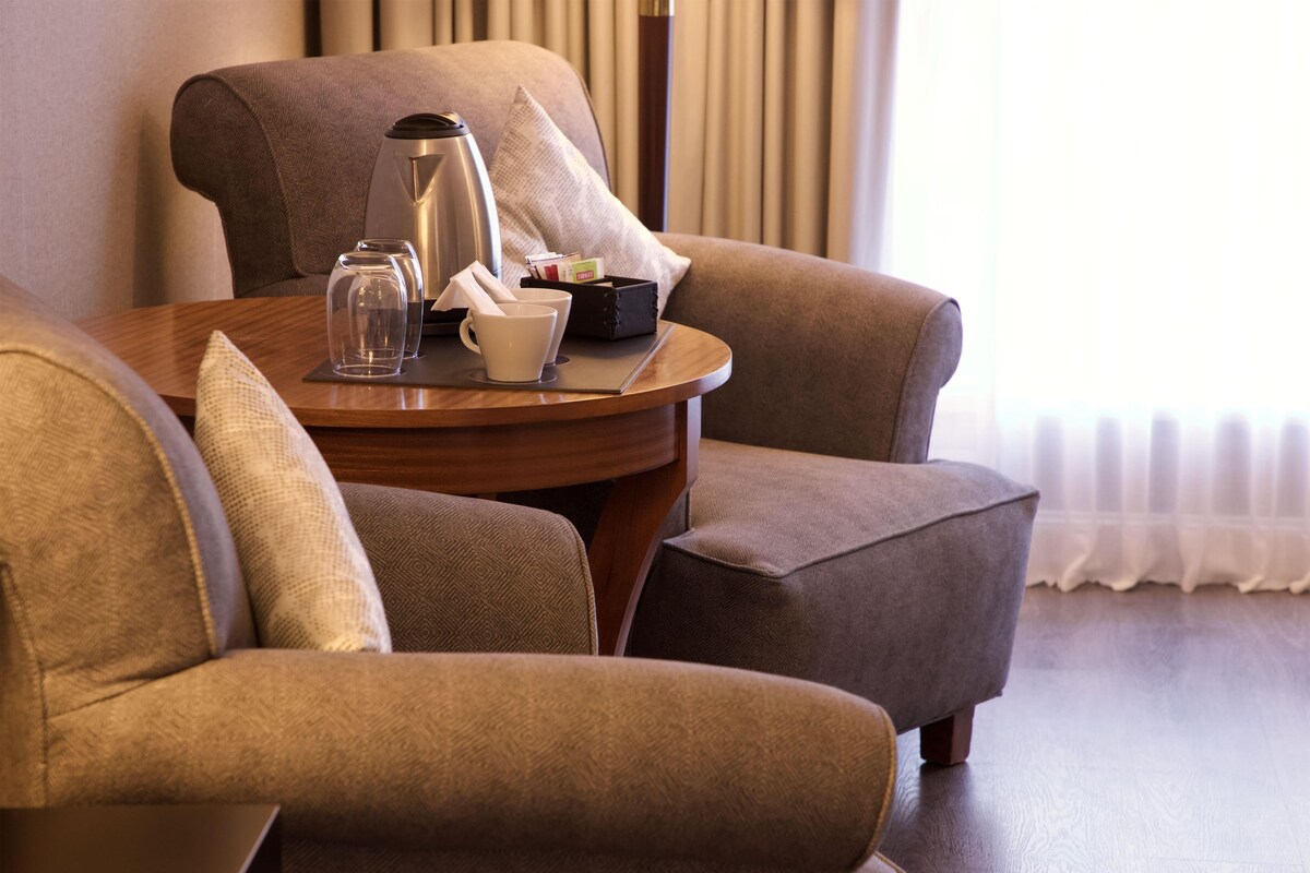 Een zithoek met een tafel, twee stoelen, een koffiezetapparaat, bekers en een klein kastje, waarschijnlijk met voorzieningen.