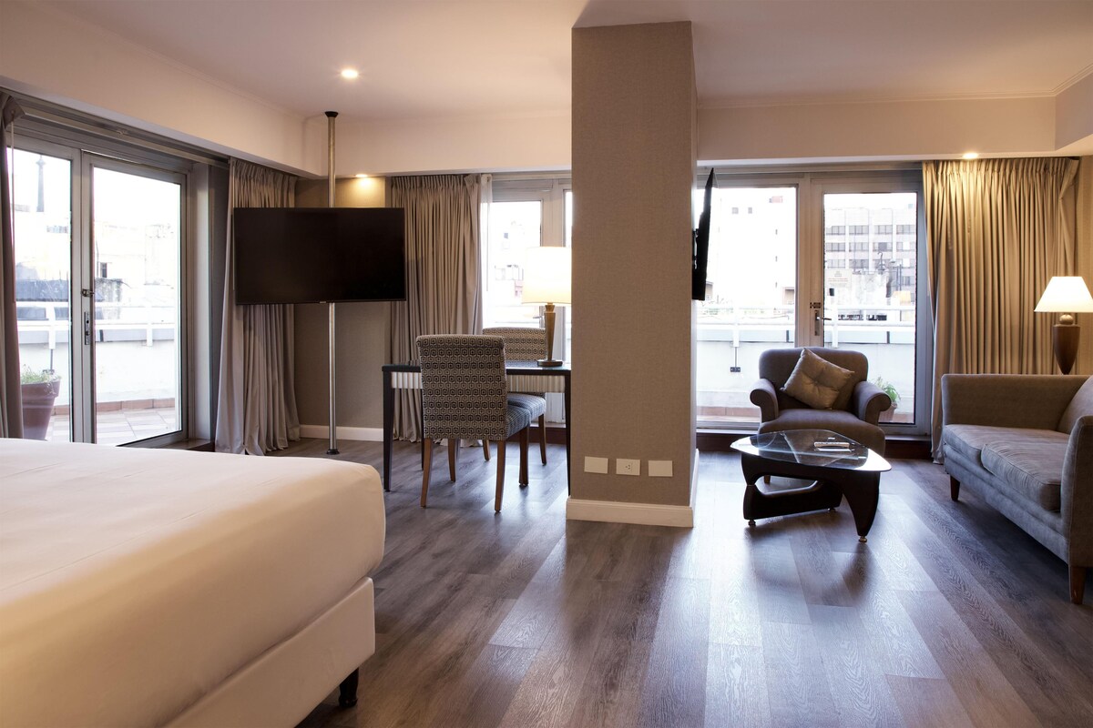 Een hotelkamer met een bed, een bureau met stoel, een bank, een salontafel en een televisie.