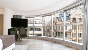 A modern bedroom with a large curved window, a flat-screen TV, and a bed with a gray blanket. - DoubleTree by Hilton Buenos Aires (Buenos Aires)