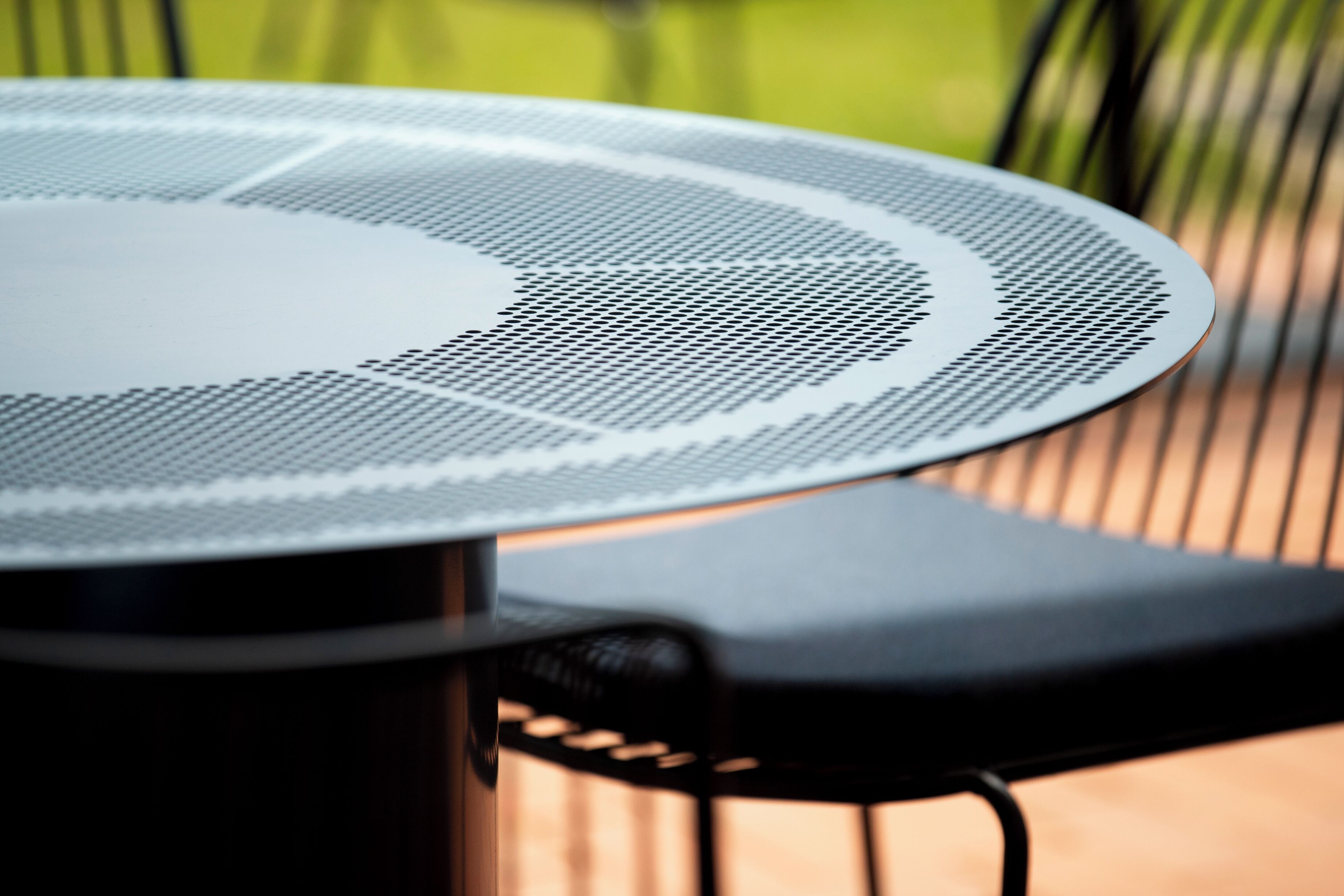 A round table with a perforated surface, likely a table fan, and a black chair with a curved backrest.