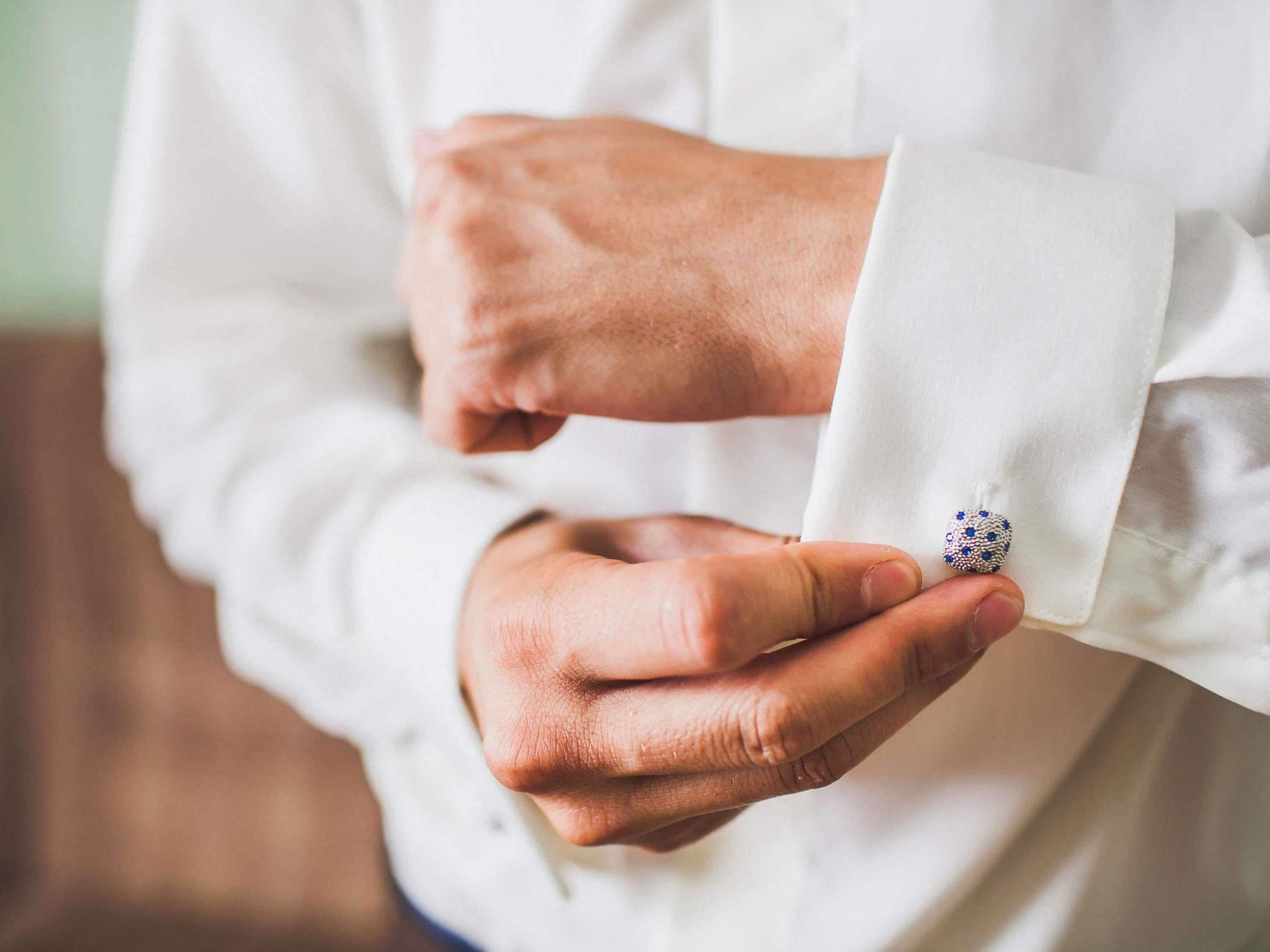 A person adjusting a cufflink on a white shirt.