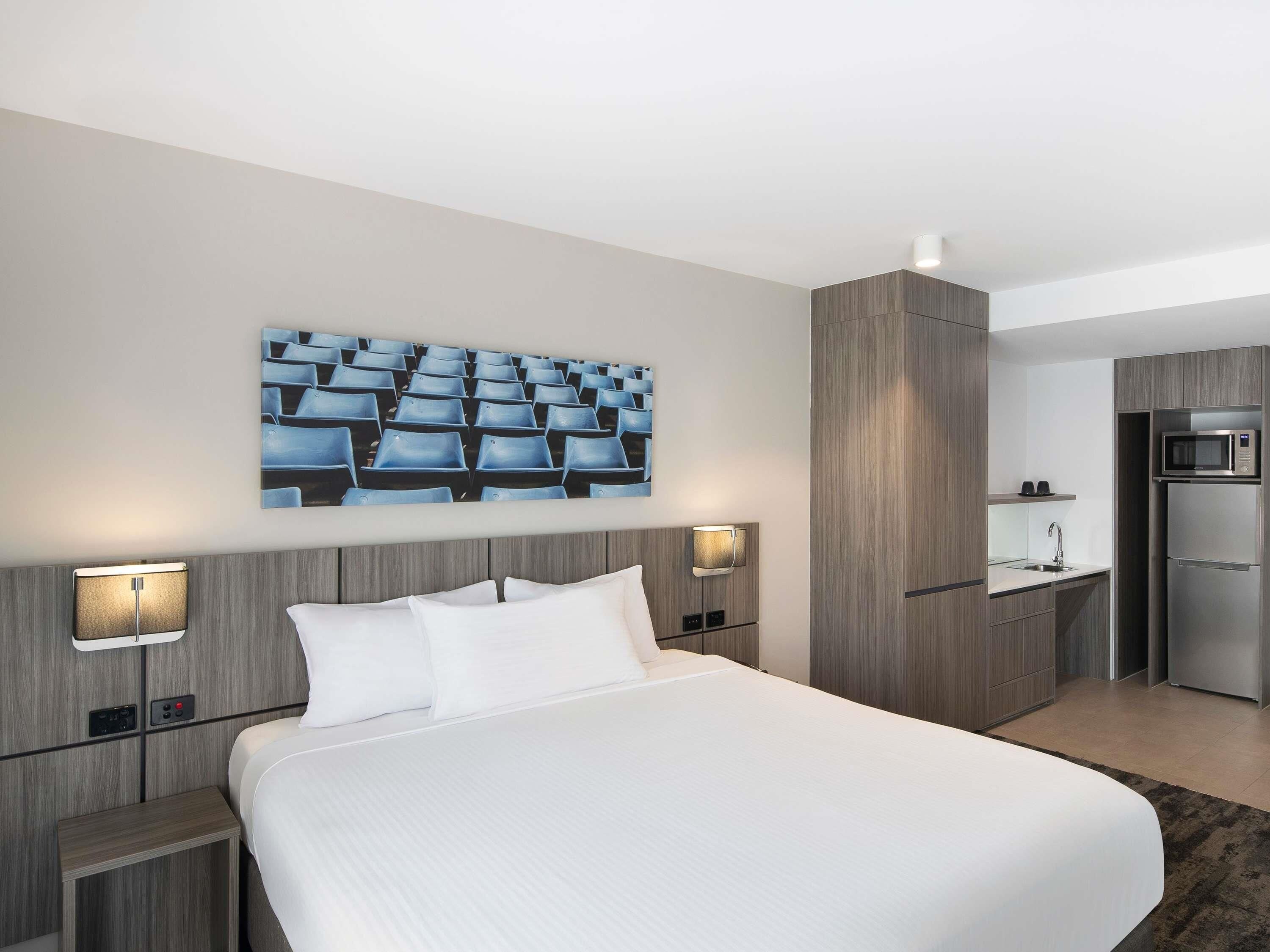A hotel room with a large bed, bedside tables, a wall-mounted TV, a microwave, and a small kitchenette.