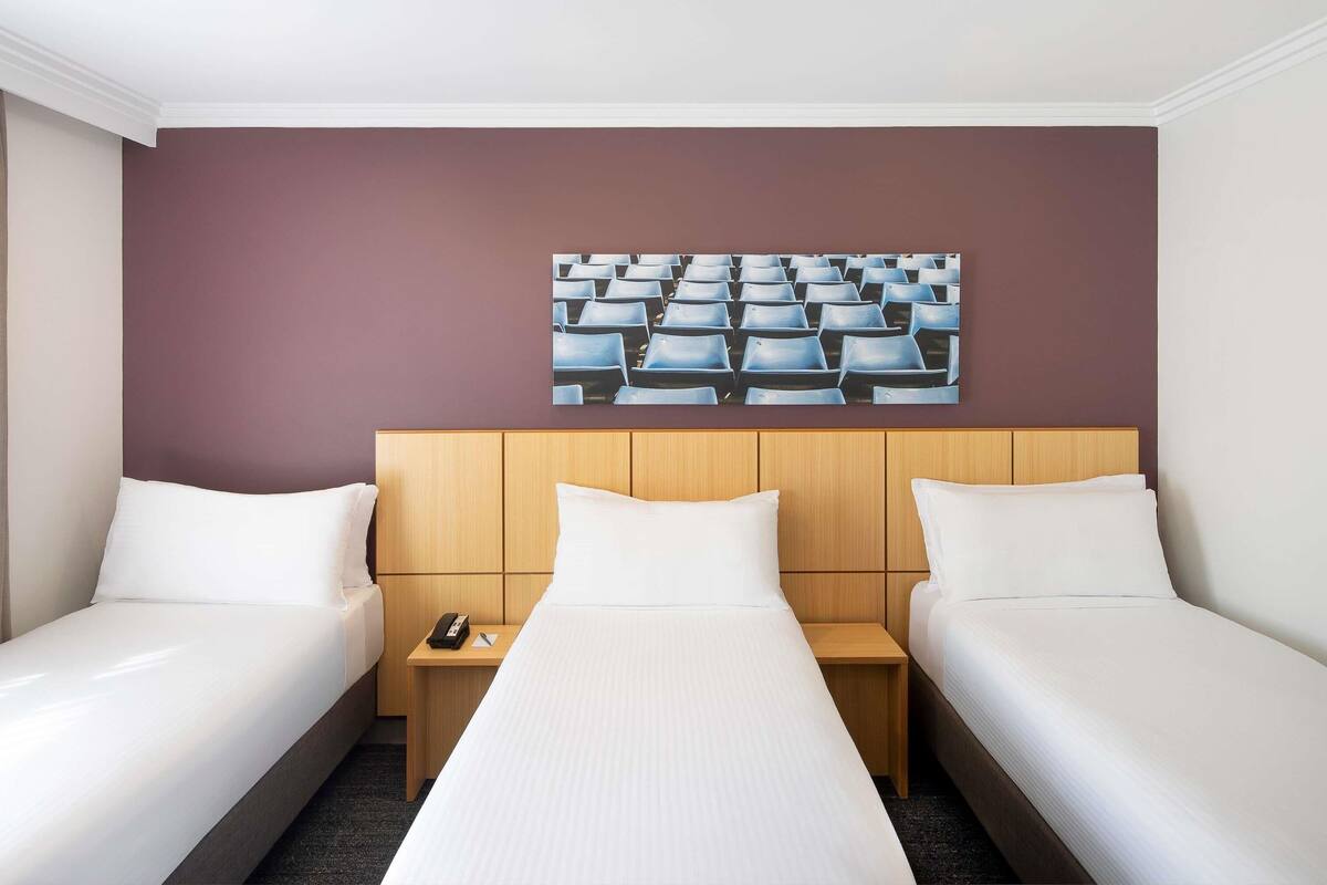 Ein Hotelzimmer mit zwei Einzelbetten, einem Holzkopfstück, einem kleinen Nachttisch mit Telefon und einem Bild von Stühlen an der Wand.