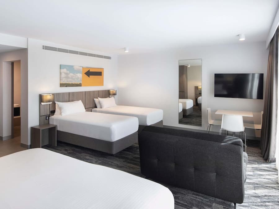 A hotel room with two beds, a desk, a TV, and a mirror.