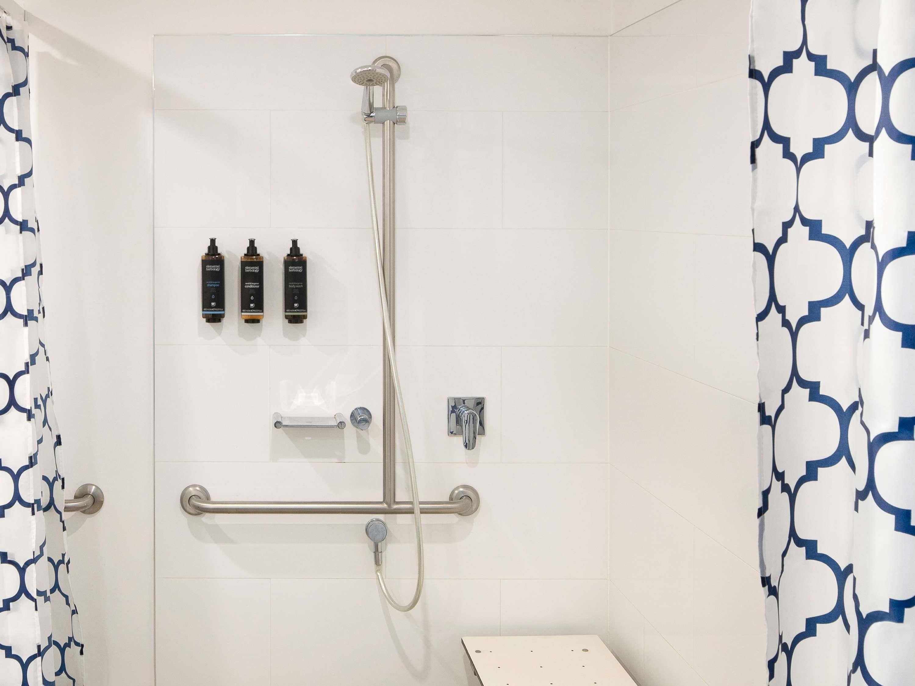 A shower area with a handheld showerhead, a handheld shower attachment, and a handheld shower nozzle. There are three bottles of shampoo and conditioner on the wall.