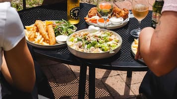 A table set outdoors with plates of food, drinks, and a bottle of beer.