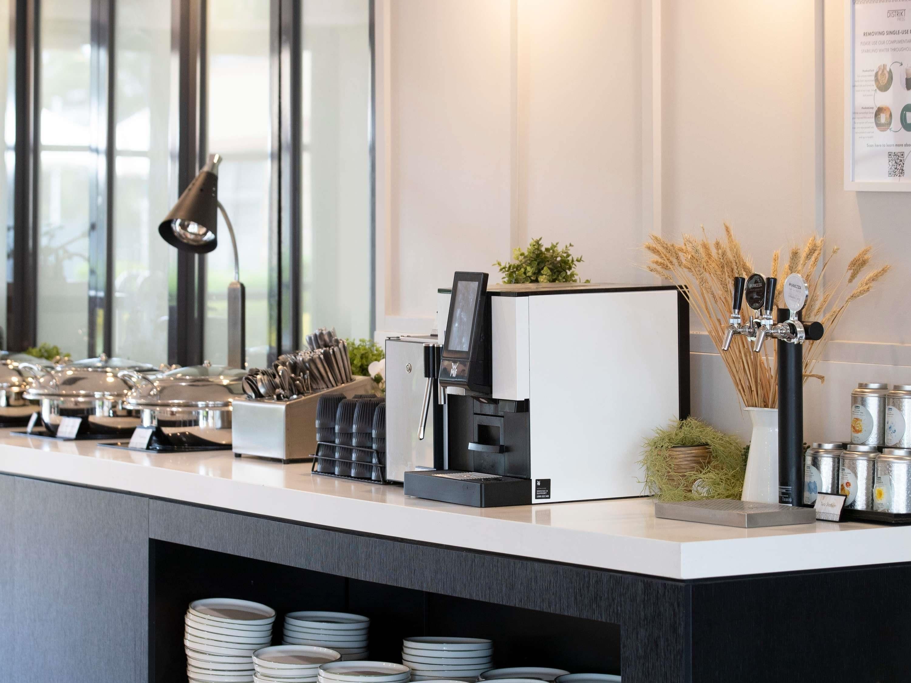 Ein Kaffee-Bereich mit einer Kaffeemaschine, einem digitalen Bildschirm sowie verschiedenen Kaffeetassen und Zubehör.
