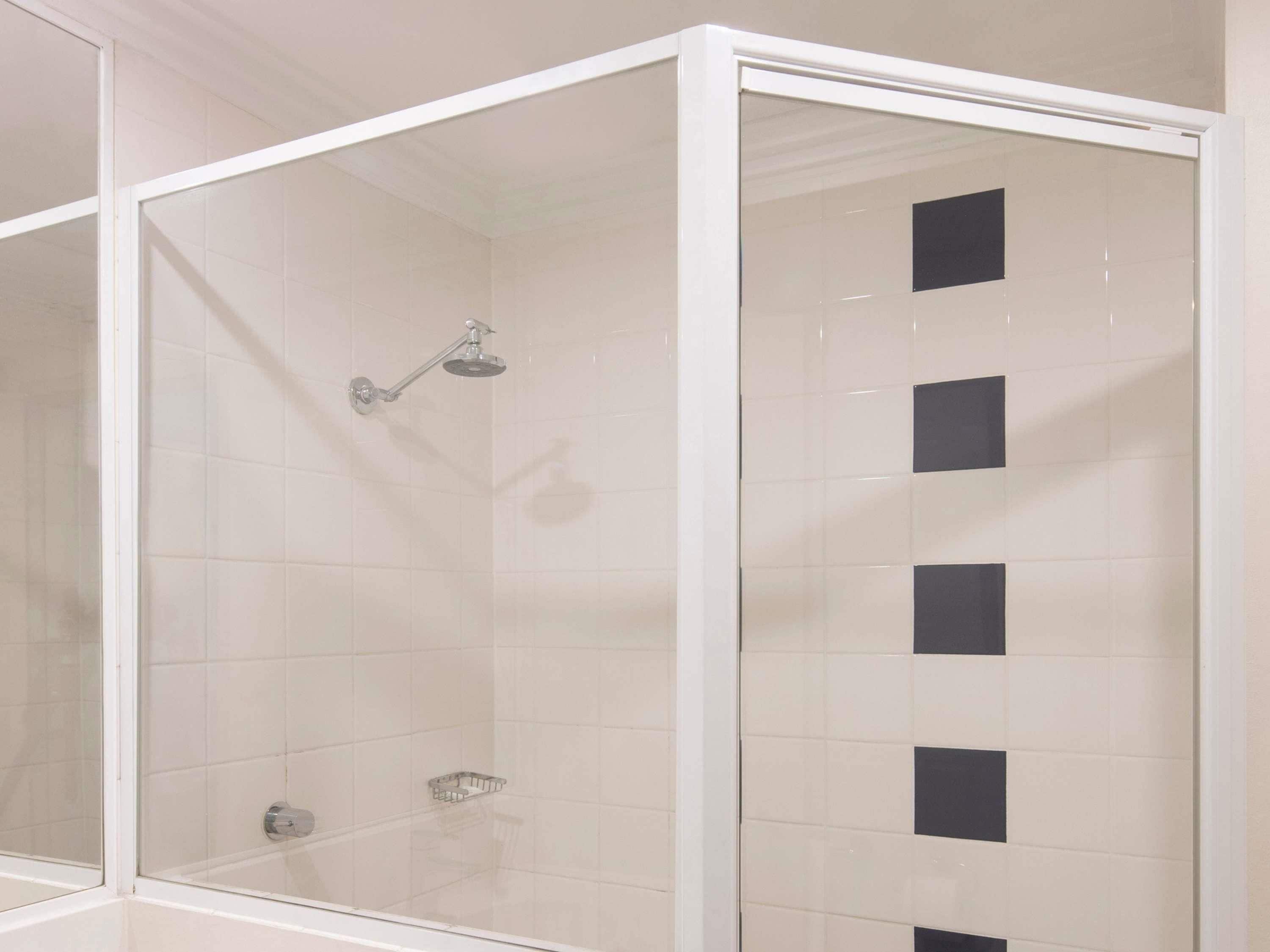 A shower enclosure with a glass door, white tiled walls, and a showerhead.