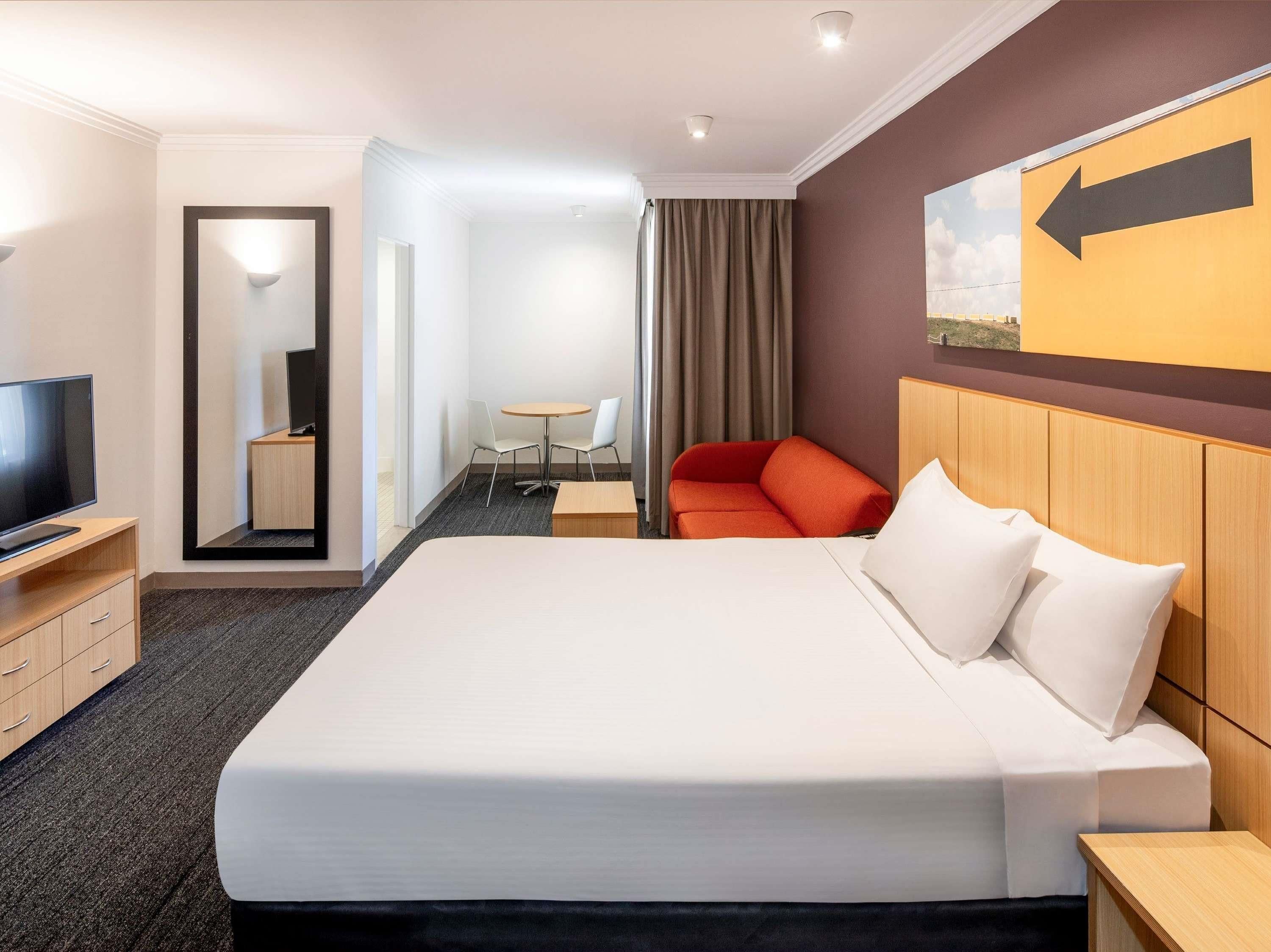 A hotel room with a large bed, a TV, a desk, and a chair.
