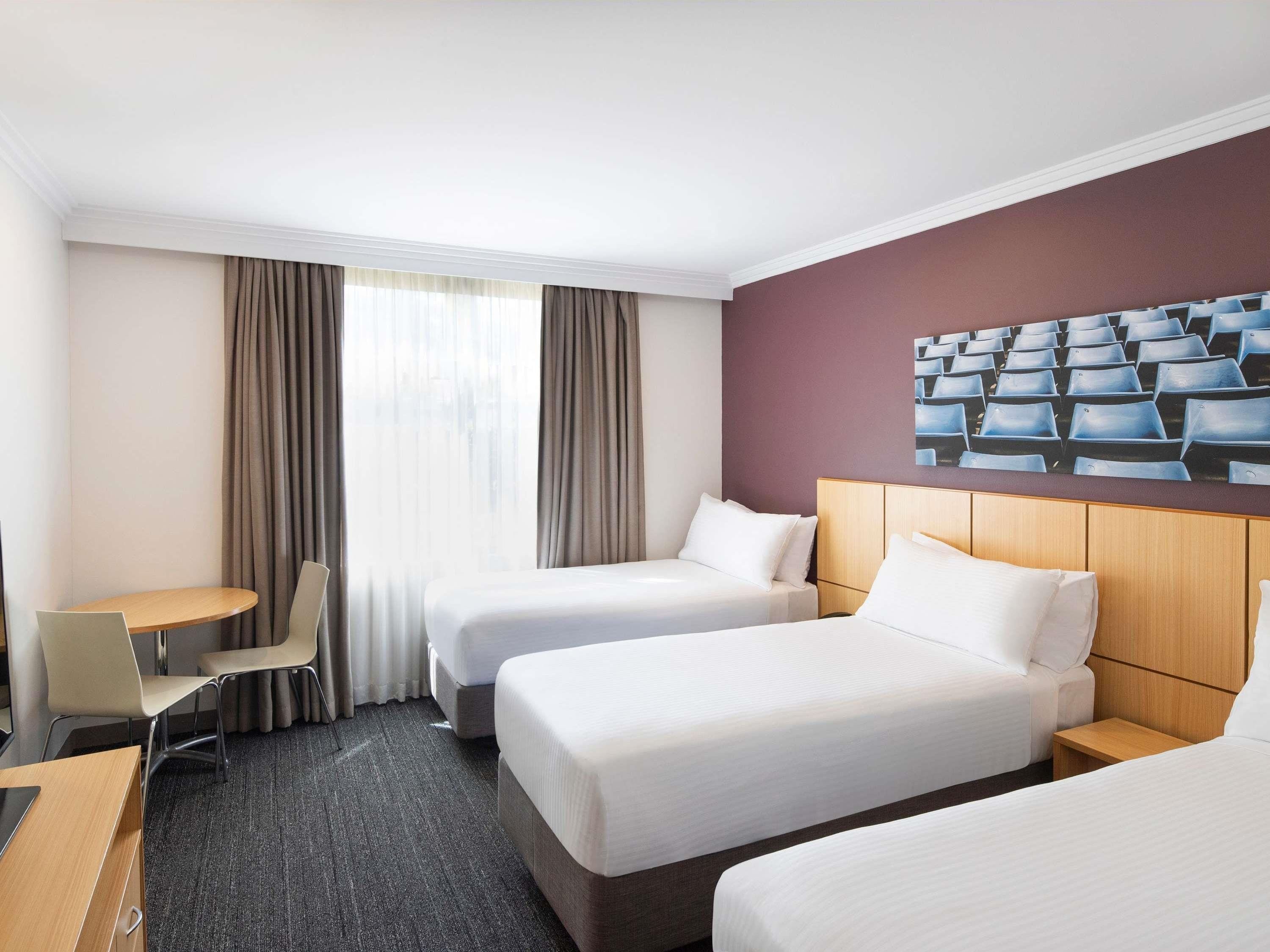 A hotel room with two beds, a desk, a chair, and a large window with curtains.