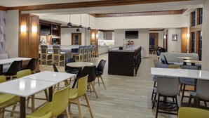A spacious dining area with multiple tables and chairs, a bar area with stools, and a kitchen in the background. - HYATT house Philadelphia/Plymouth Meeting (East Norriton)