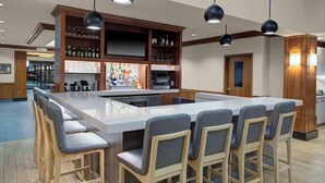 A bar area with a long counter, bar stools, and shelves stocked with bottles and glasses. - HYATT house Philadelphia/Plymouth Meeting (East Norriton)