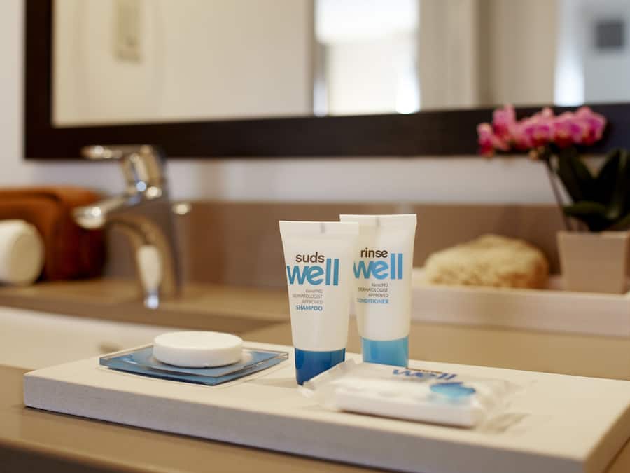 Ein Badezimmer-Waschtisch mit Schaum, Shampoo und Conditioner, eine weiße Seife und eine kleine, blaue Ablagefläche.