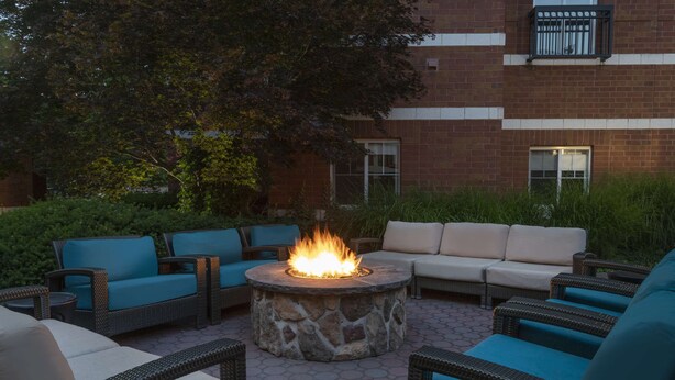 An outdoor seating area with wicker furniture and a stone fire pit. - HYATT house Philadelphia/Plymouth Meeting (East Norriton)