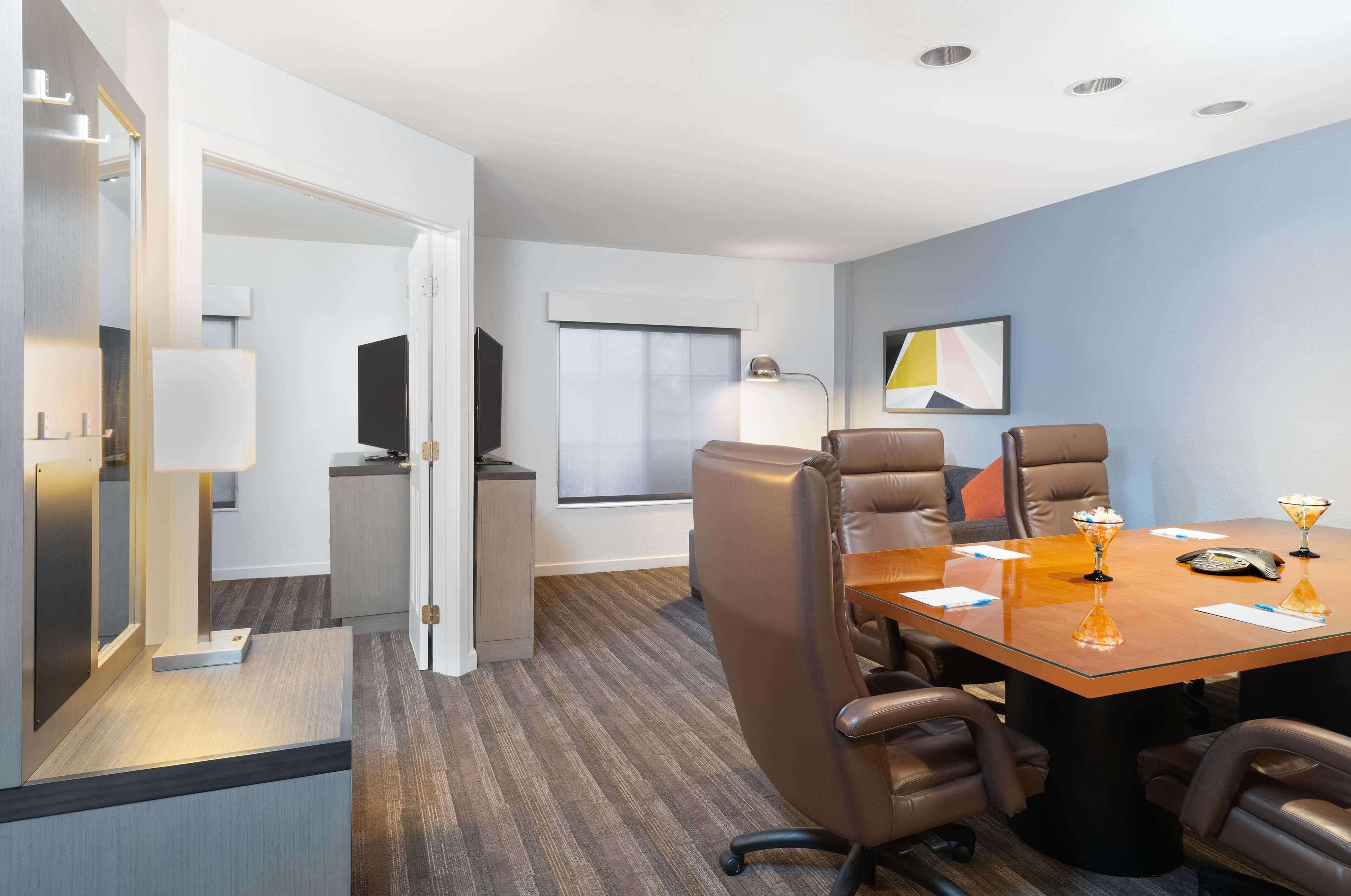 A modern conference room with a glass table, leather chairs, a television, and a window with blinds.