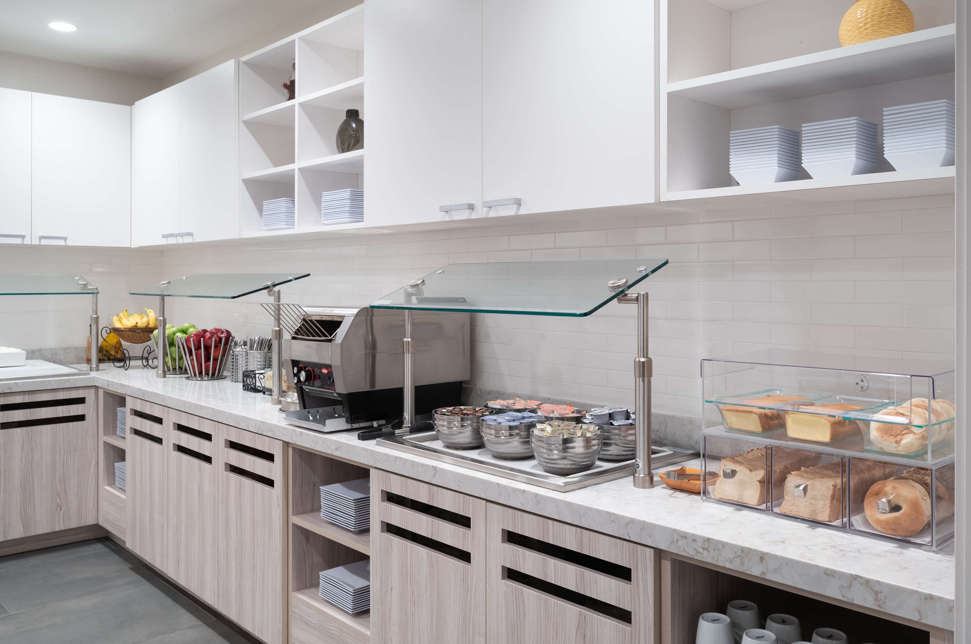 A modern kitchen with white cabinets, a marble countertop, and glass display cases for food items.