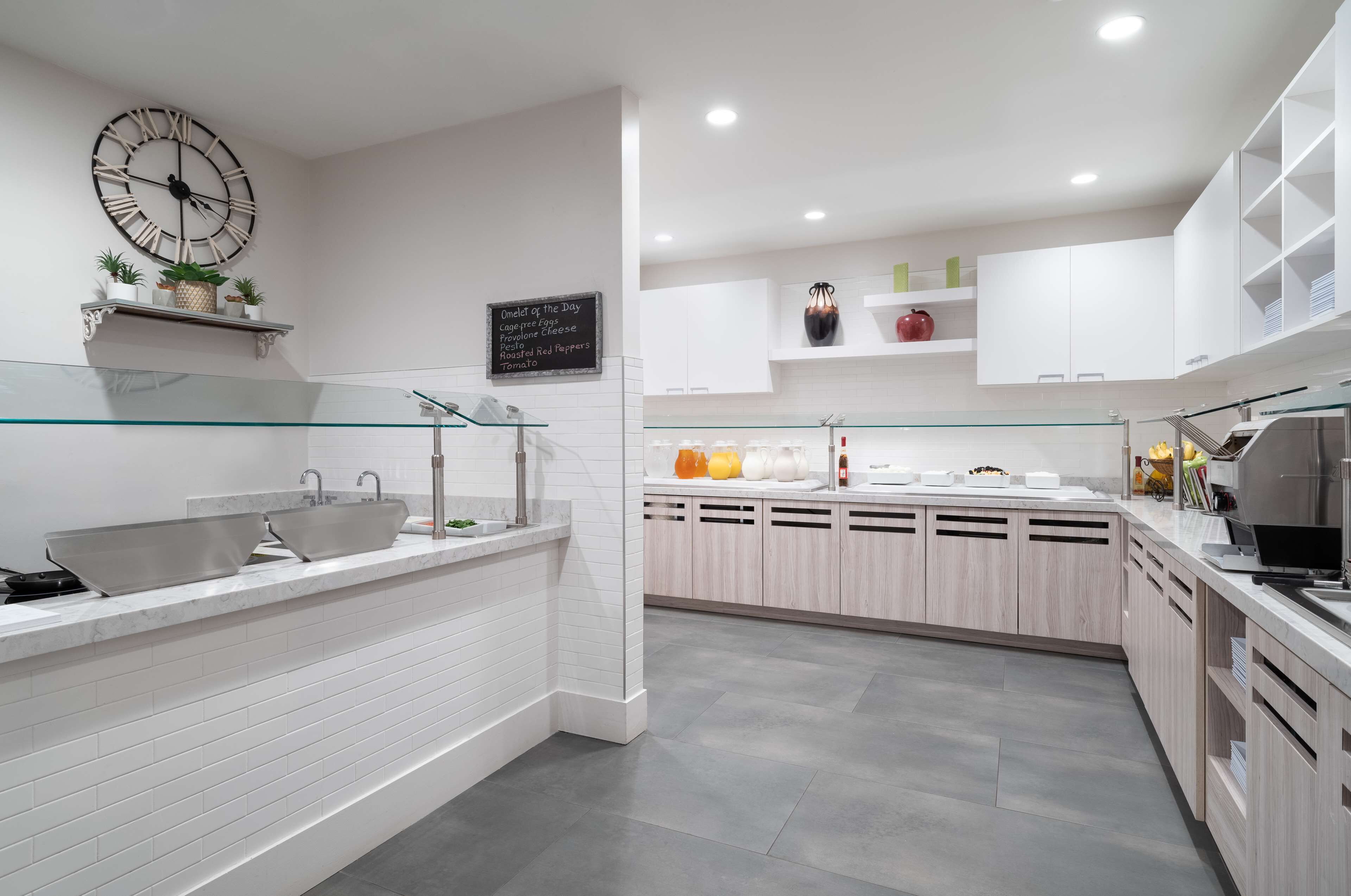 A modern kitchen with white cabinetry, a large clock, and a glass backsplash.
