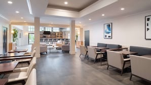 Een ruime eetruimte met diverse zitmogelijkheden, zoals zitjes en tafels, een keuken op de achtergrond en een modern interieur.