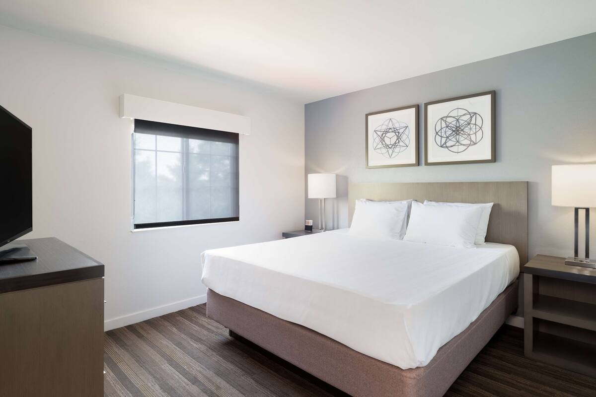 Een hotelkamer met een groot bed, een flatscreen televisie, een raam en twee wandlampen.