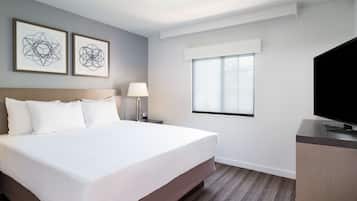 A hotel room with a large bed, a desk with a TV, a window, and two framed artworks on the wall.