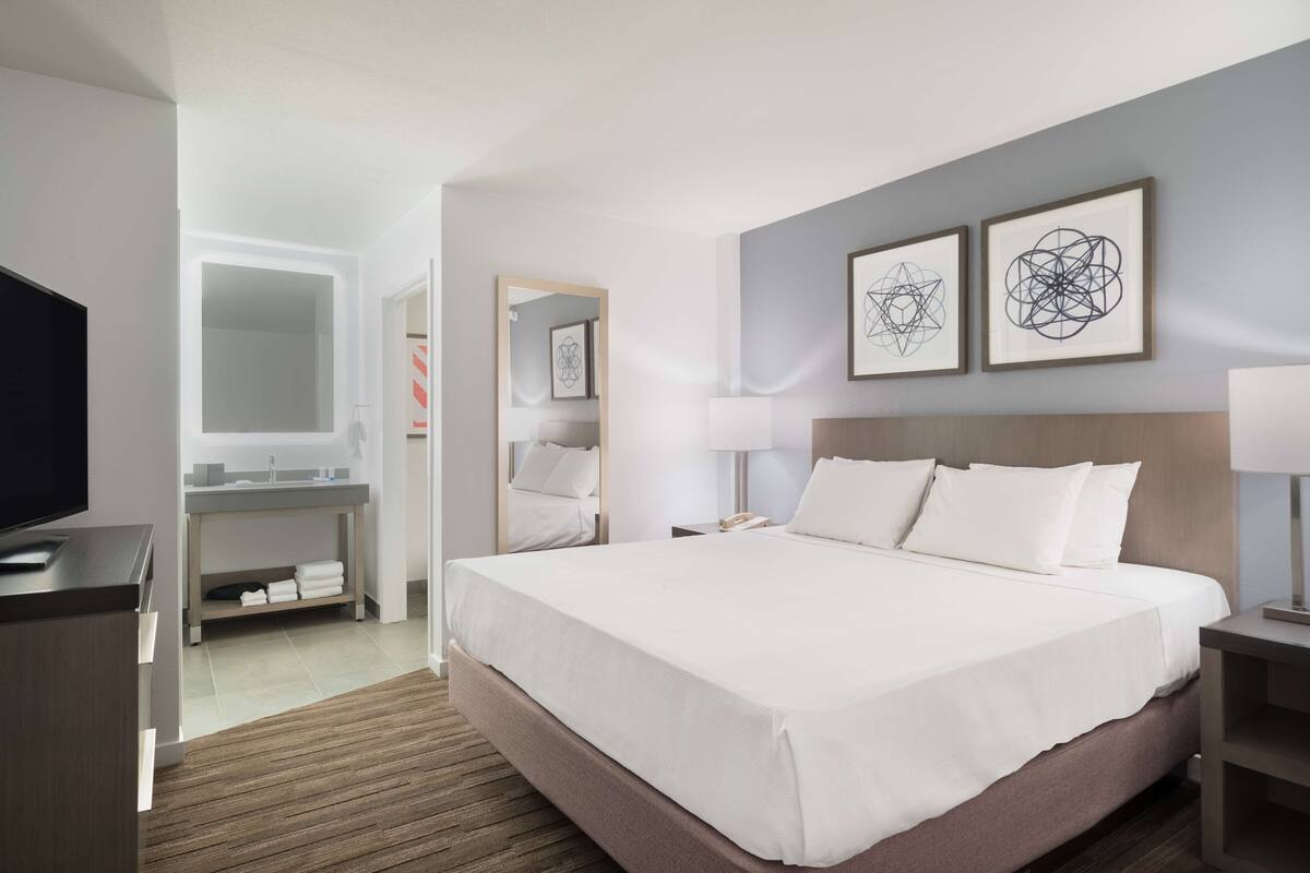 Een moderne hotelkamer met een groot bed, een televisie, een bureau met een computer en een badkamer met een spiegel en wastafel.