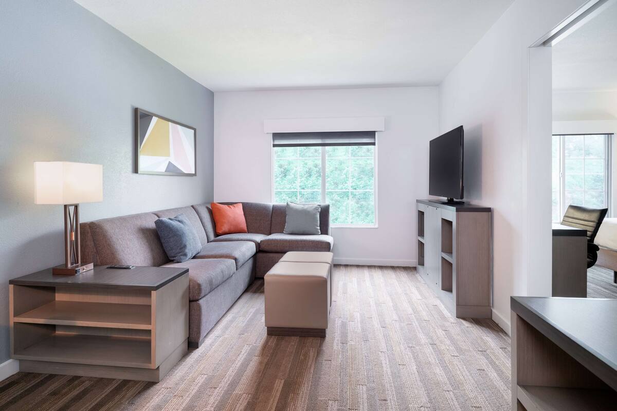 Een moderne woonkamer met een hoekbank, een flatscreen televisie, een salontafel en een bijzettafeltje met een lamp.