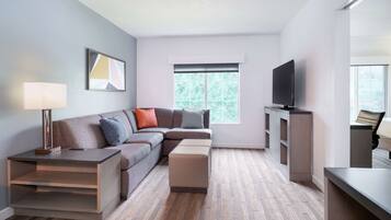 A modern living room with a sectional sofa, a flat-screen TV, a coffee table, and a side table with a lamp.