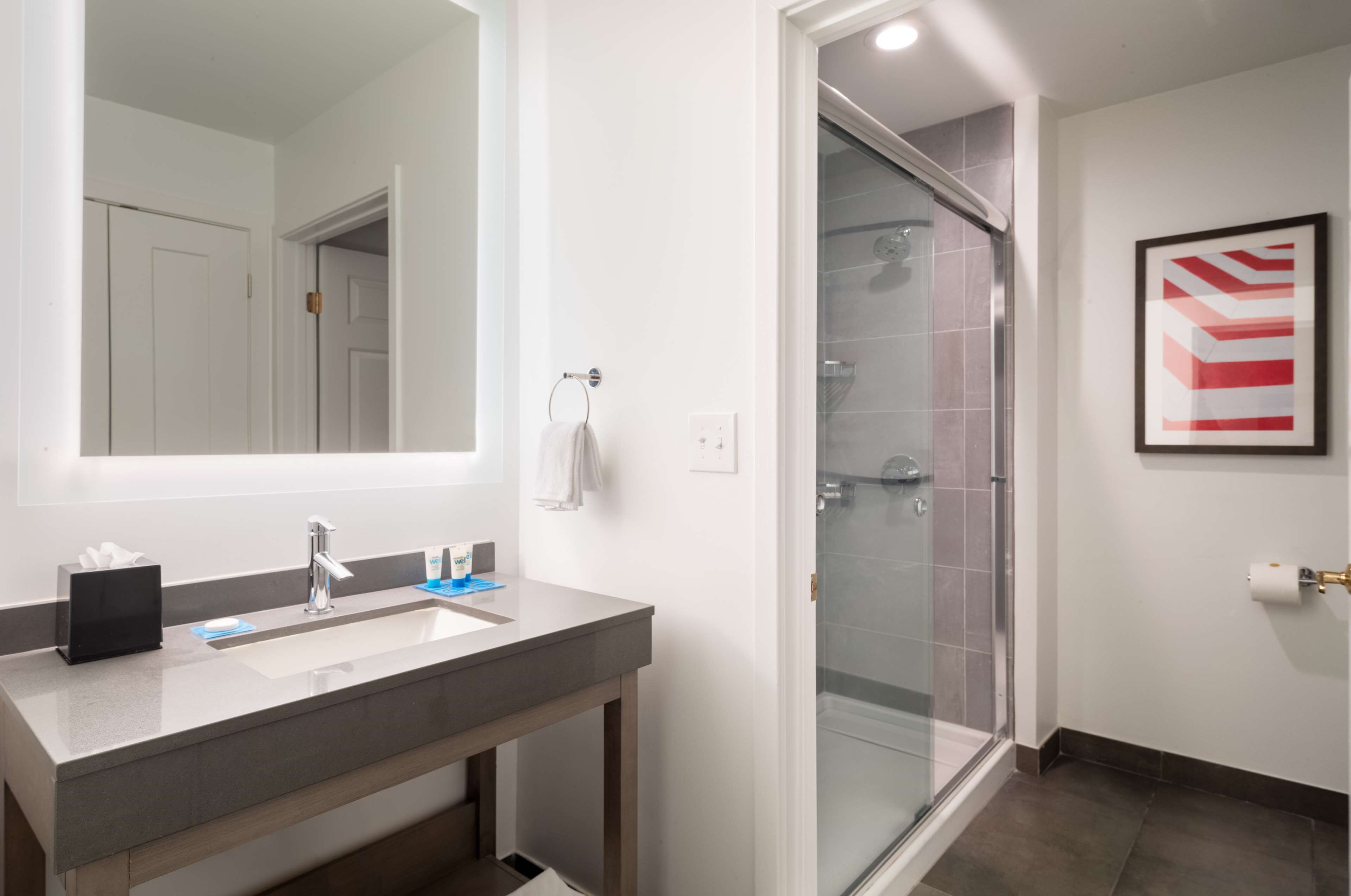 A modern bathroom with a large mirror, a sink, and a glass shower enclosure.