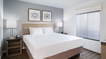 A hotel room with a large bed, two bedside tables with lamps, a window with blinds, and two framed abstract wall art pieces.