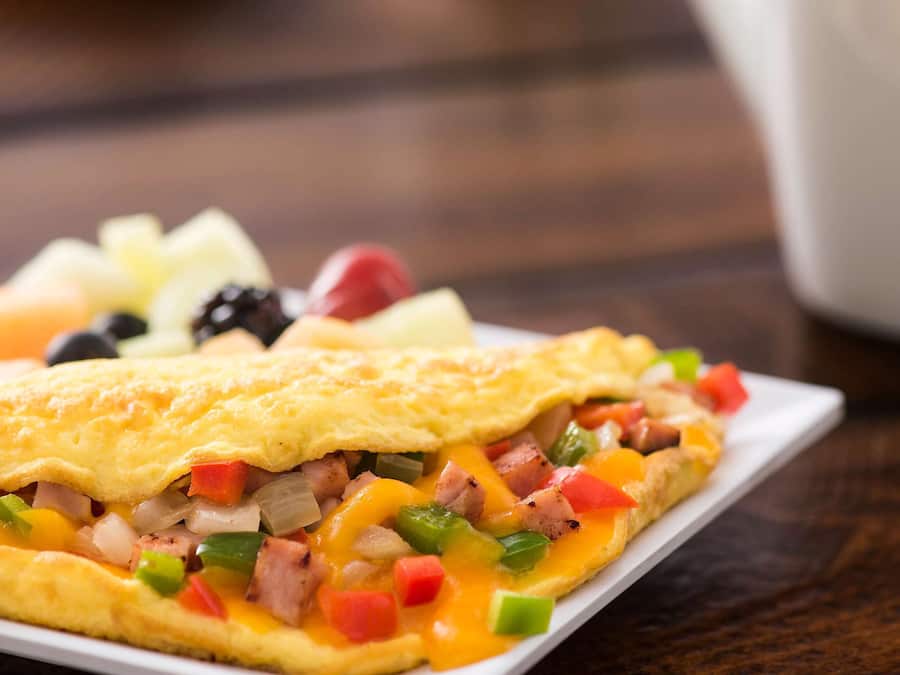 Een ontbijt bord met een omelet, gehakte groenten en fruit.