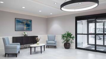 A modern lobby with two armchairs, a round table, a potted plant, and a large abstract painting on the wall.