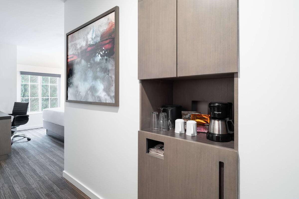 Een moderne kantoorruimte met een groot abstract schilderij, een koffiehoek en een bureau met stoel.
