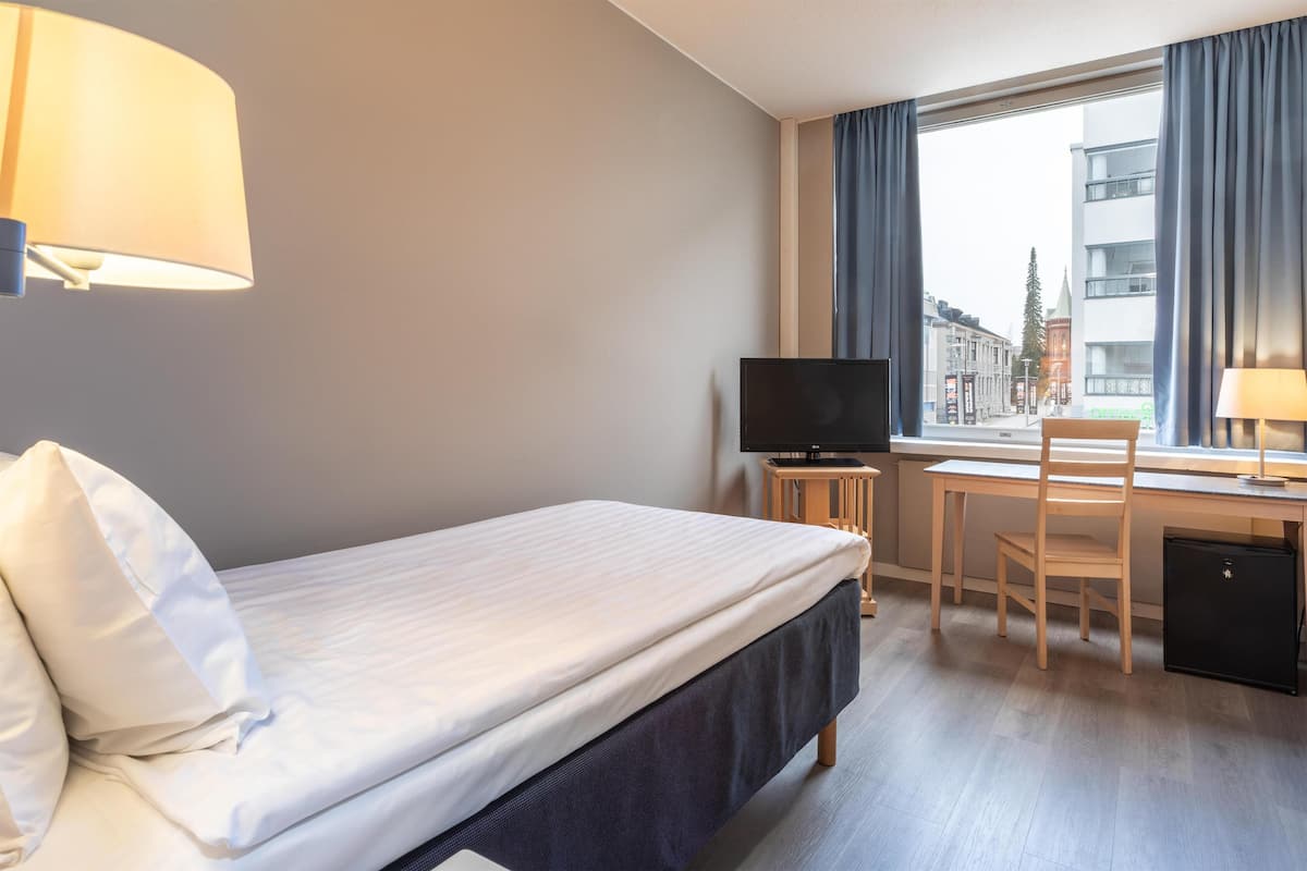 A hotel room with a bed, a desk, a chair, a television, and a window with curtains.