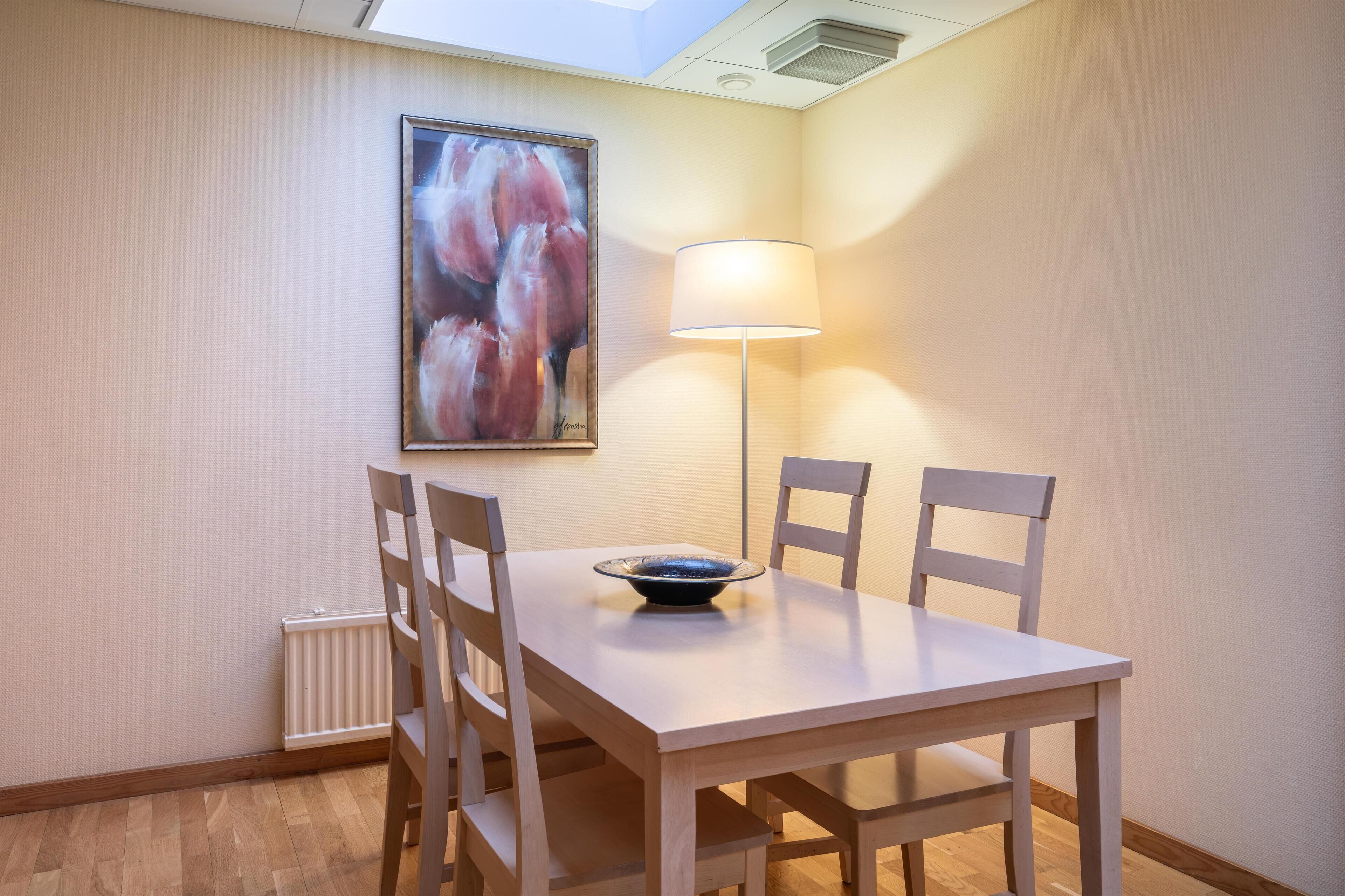 Un comedor con una mesa, sillas, un cuenco, una lámpara y un cuadro en la pared.
