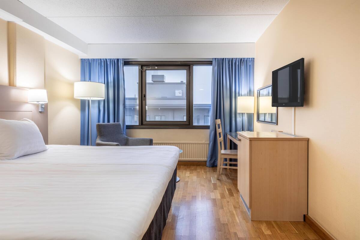 A hotel room with a bed, desk, chair, TV, and a window with curtains.