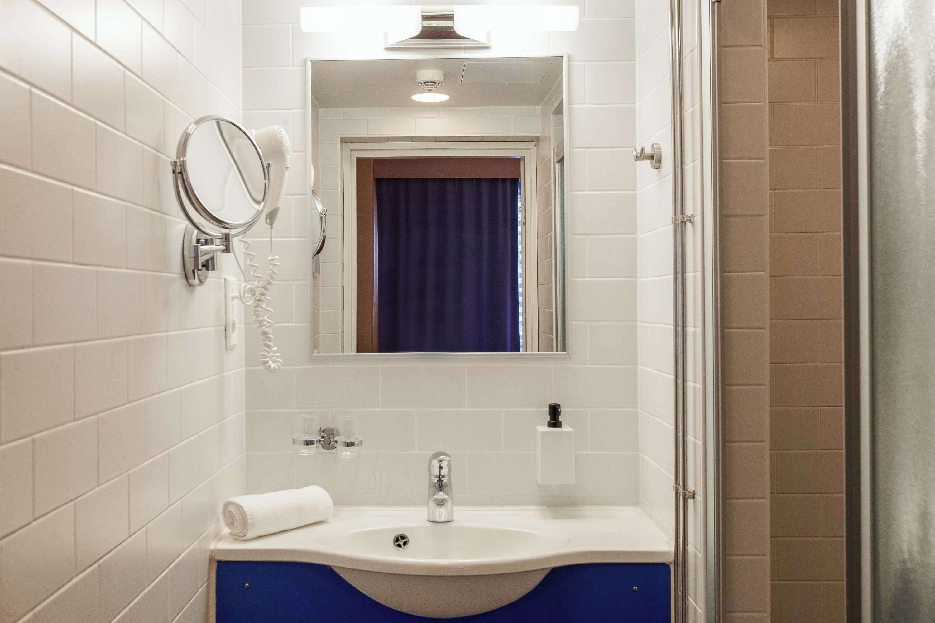 A bathroom with a white sink, a mirror, a hairdryer, and a blue curtain.