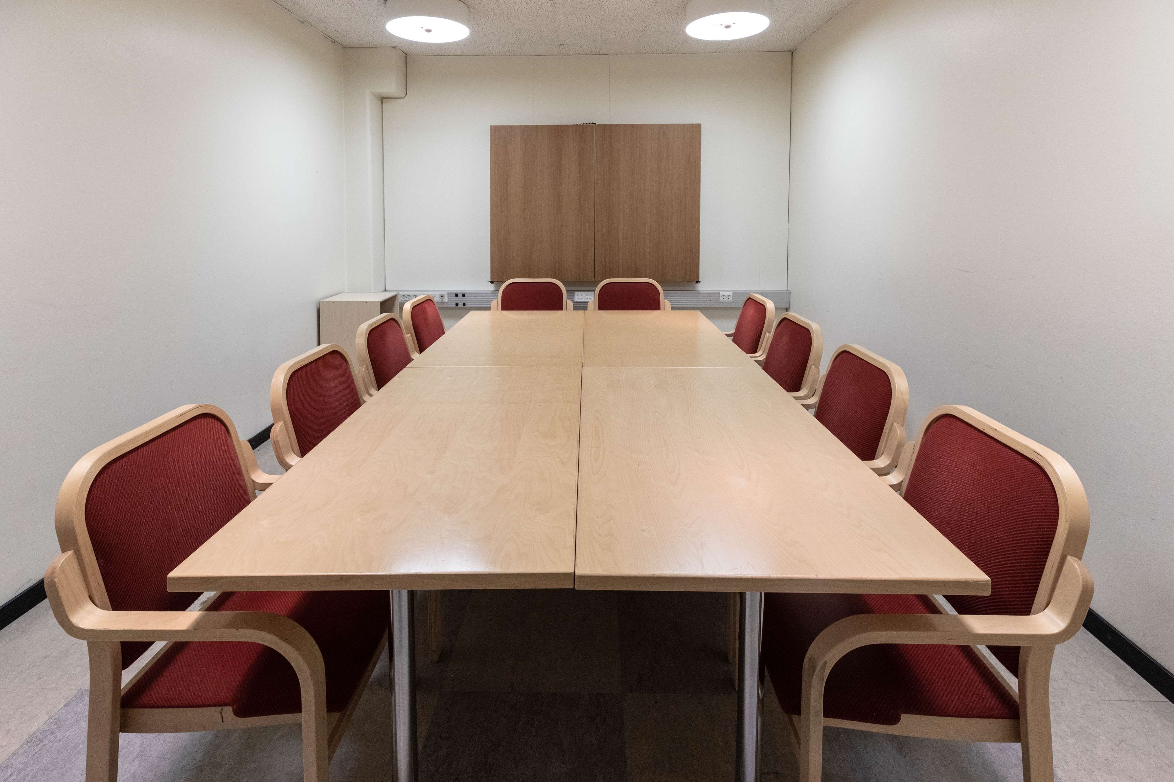 Un salón de conferencias con una larga mesa y sillas tapizadas en rojo.