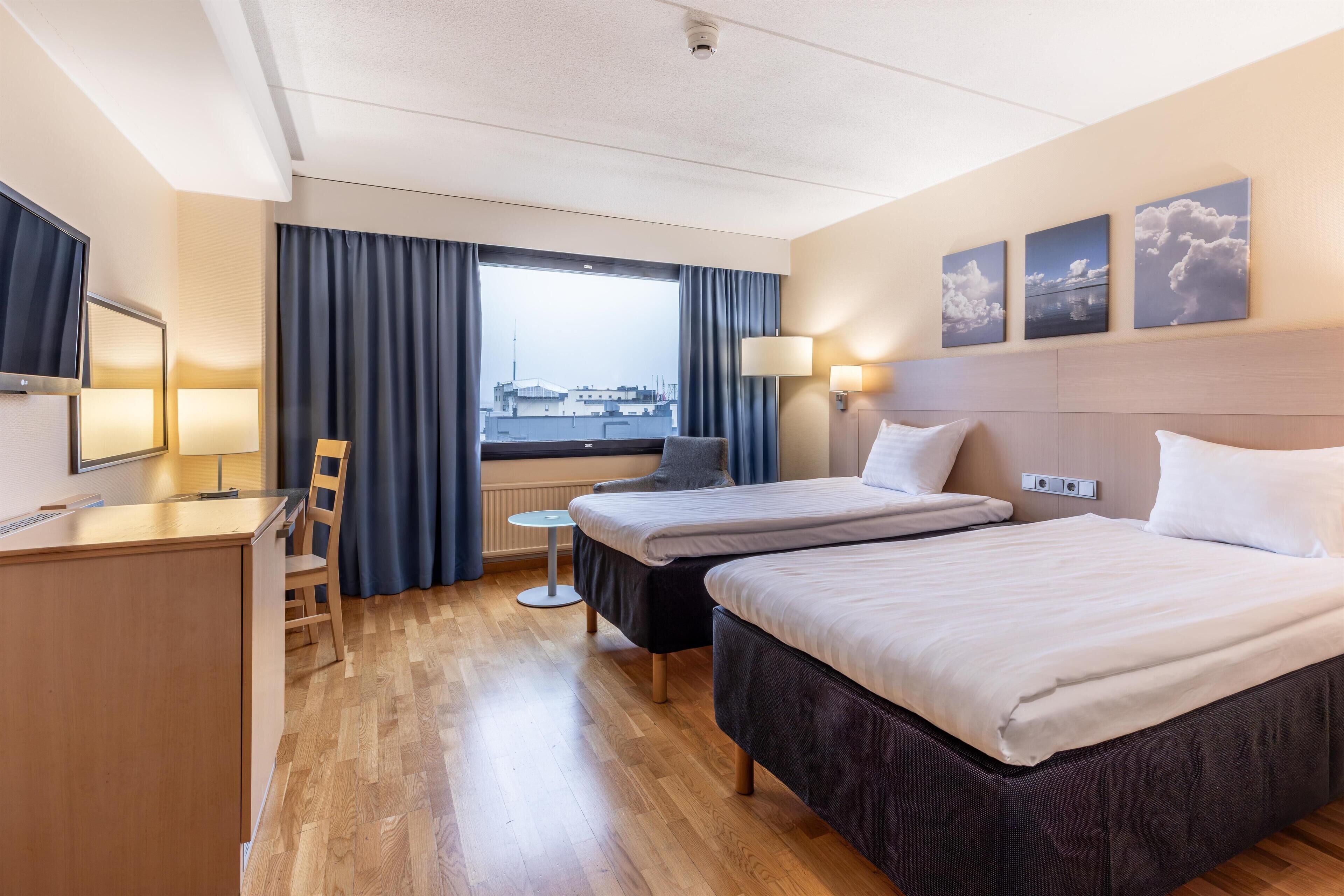 A hotel room with two beds, a desk, a chair, a small table, and a window with curtains.
