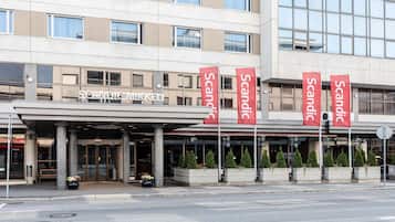 Scandic Market hotel features a modern design with a flat roof and large windows, a covered entrance with flags, and potted plants.