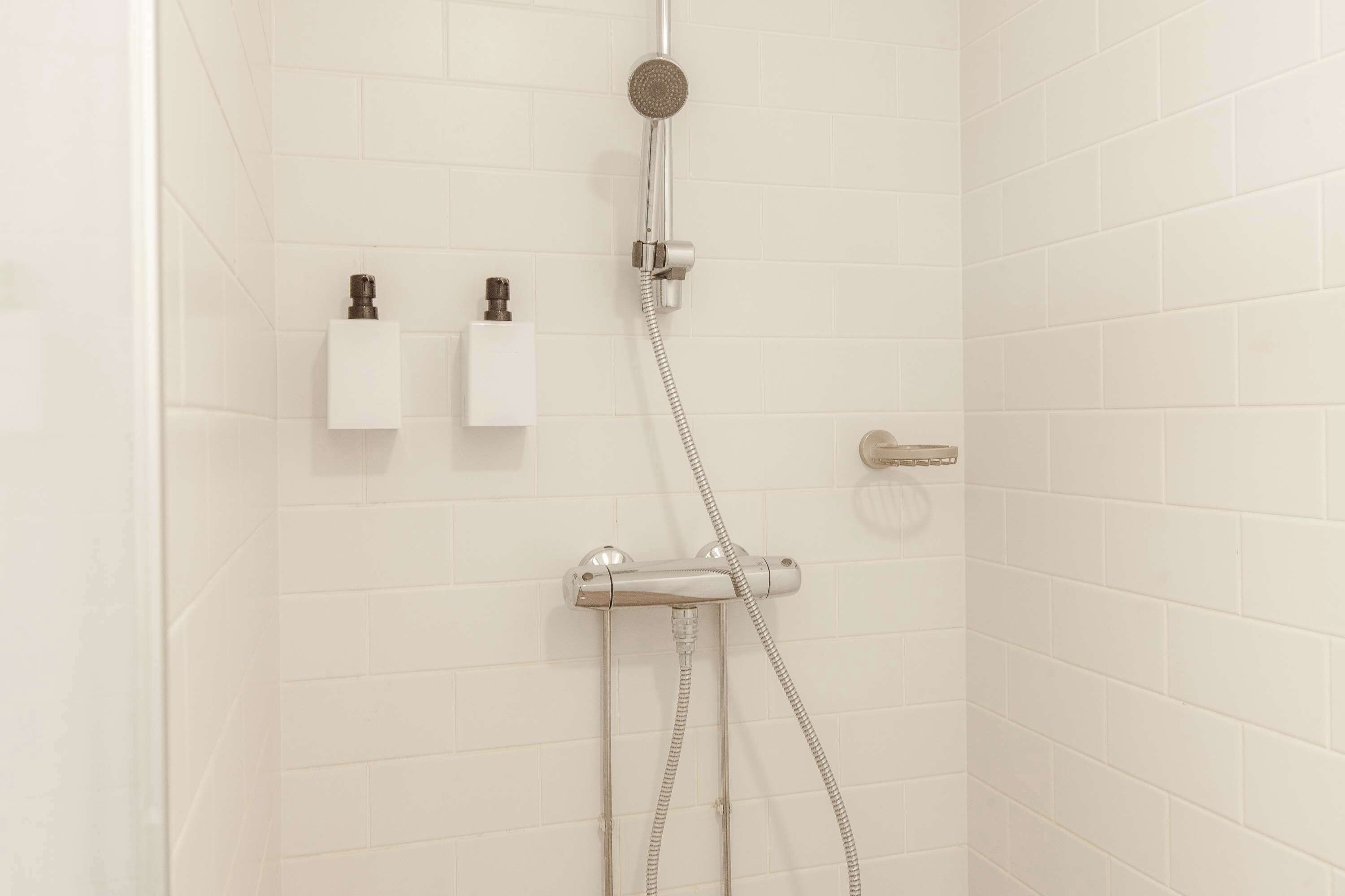 Eine Dusche mit Duschbrause und Wandarmatur. Zwei Seifenspender sind an der Wand angebracht.