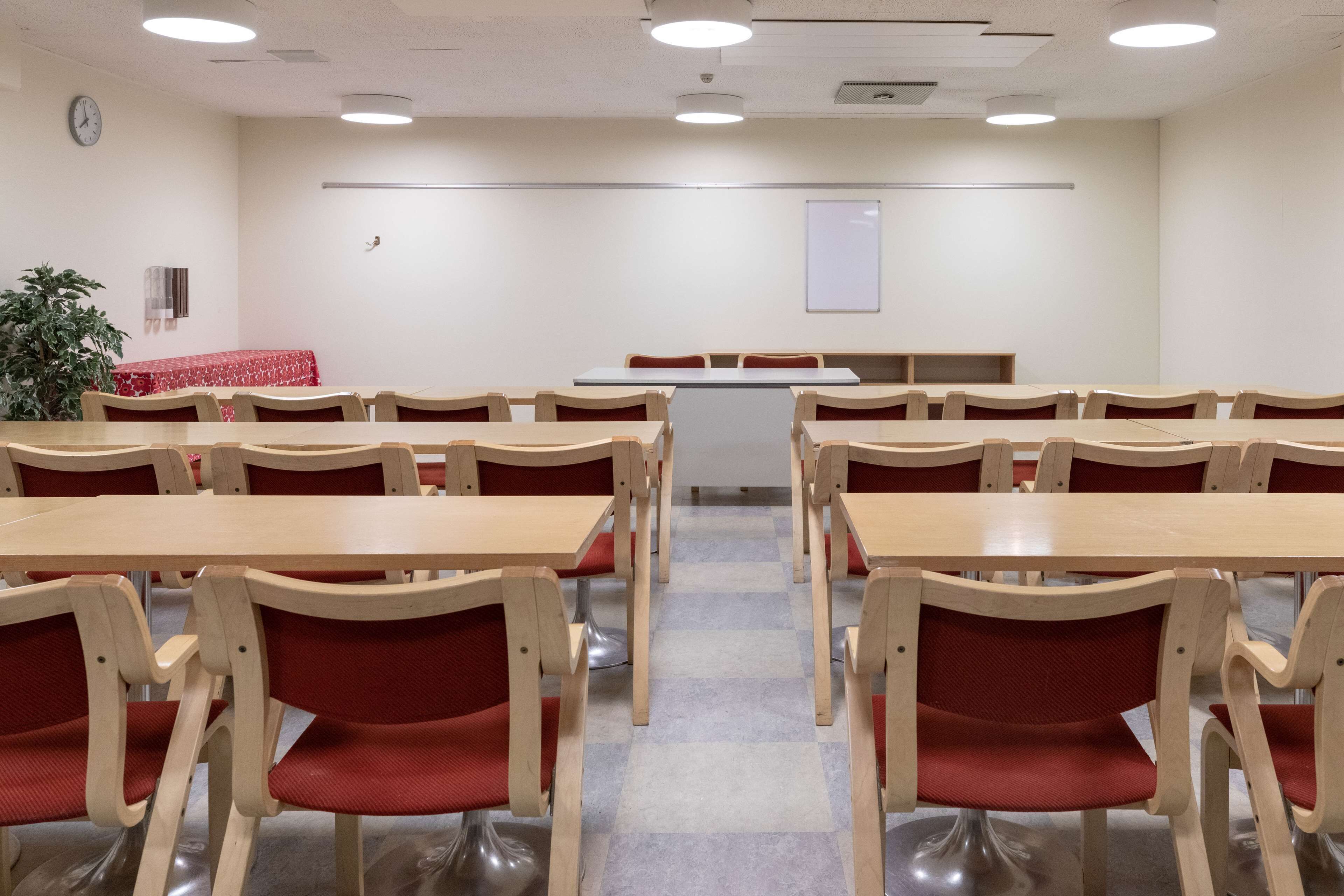 A conference room with wooden tables and red chairs, a clock on the wall, and a whiteboard.