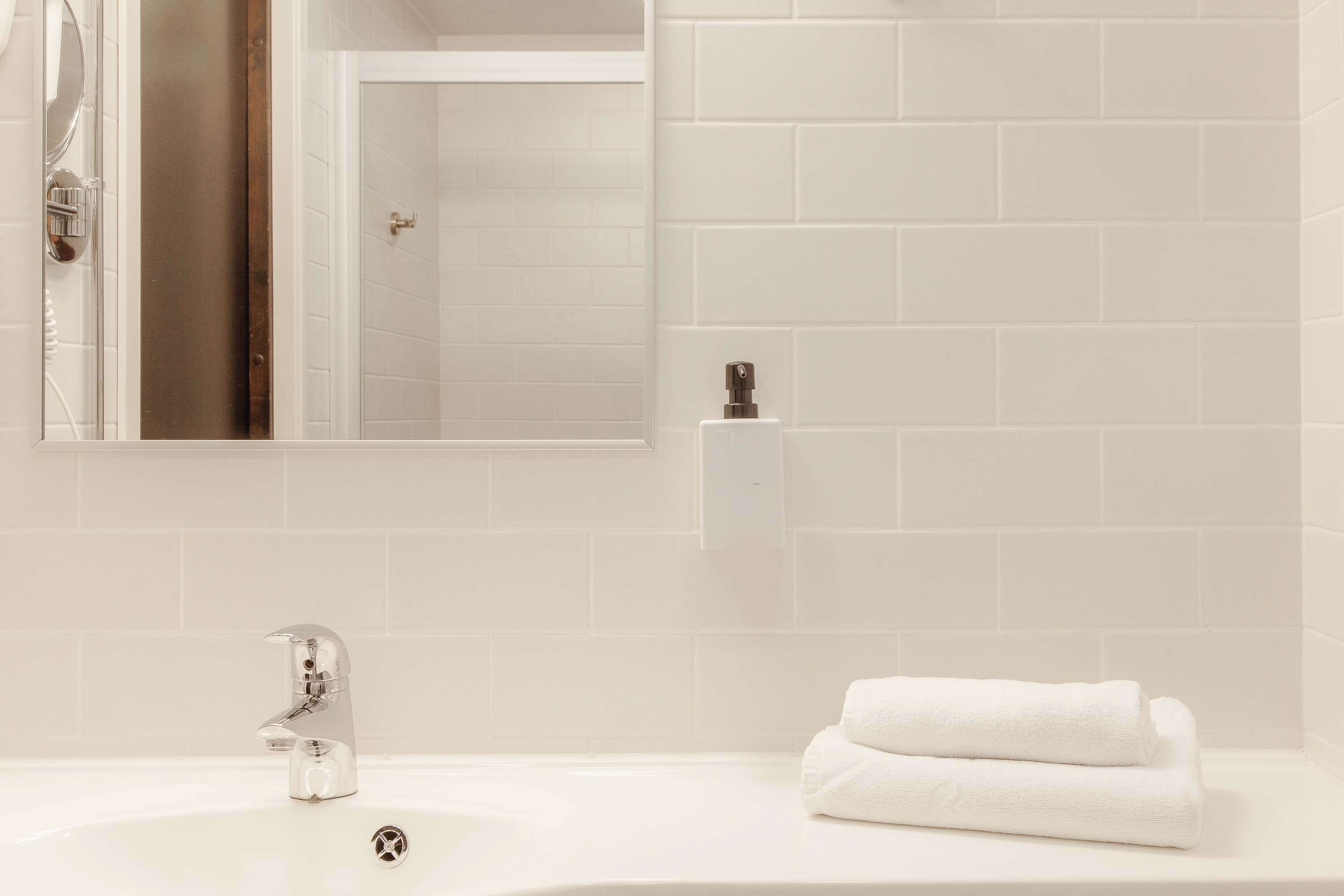 A bathroom with a white sink, a modern faucet, a mirror, and a towel.