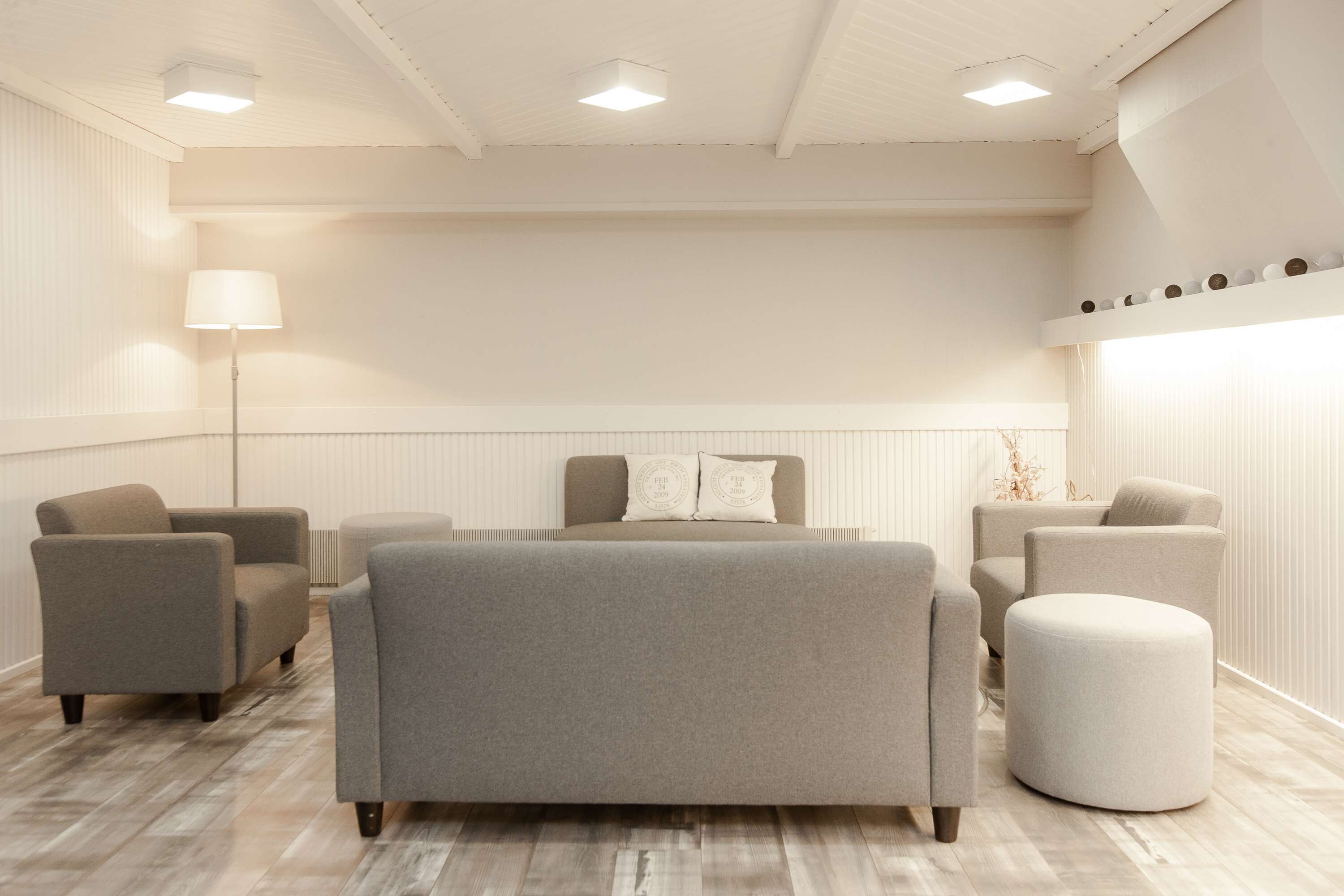A modern bedroom with a large bed, two armchairs, a round ottoman, and a floor lamp.