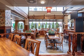 A restaurant with wooden tables and chairs, large windows, and a view of trees outside. - Scandic Mikkeli (Mikkeli)