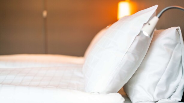 A neatly made bed with white bedding and pillows, a bedside lamp, and a wall-mounted light fixture. - Scandic Mikkeli (Mikkeli)