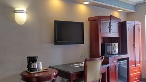 A hotel room with a flat-screen TV mounted on the wall, a small table with a coffee maker, and a microwave on a cabinet. - Destiny Palms Hotel Maingate West (Kissimmee)