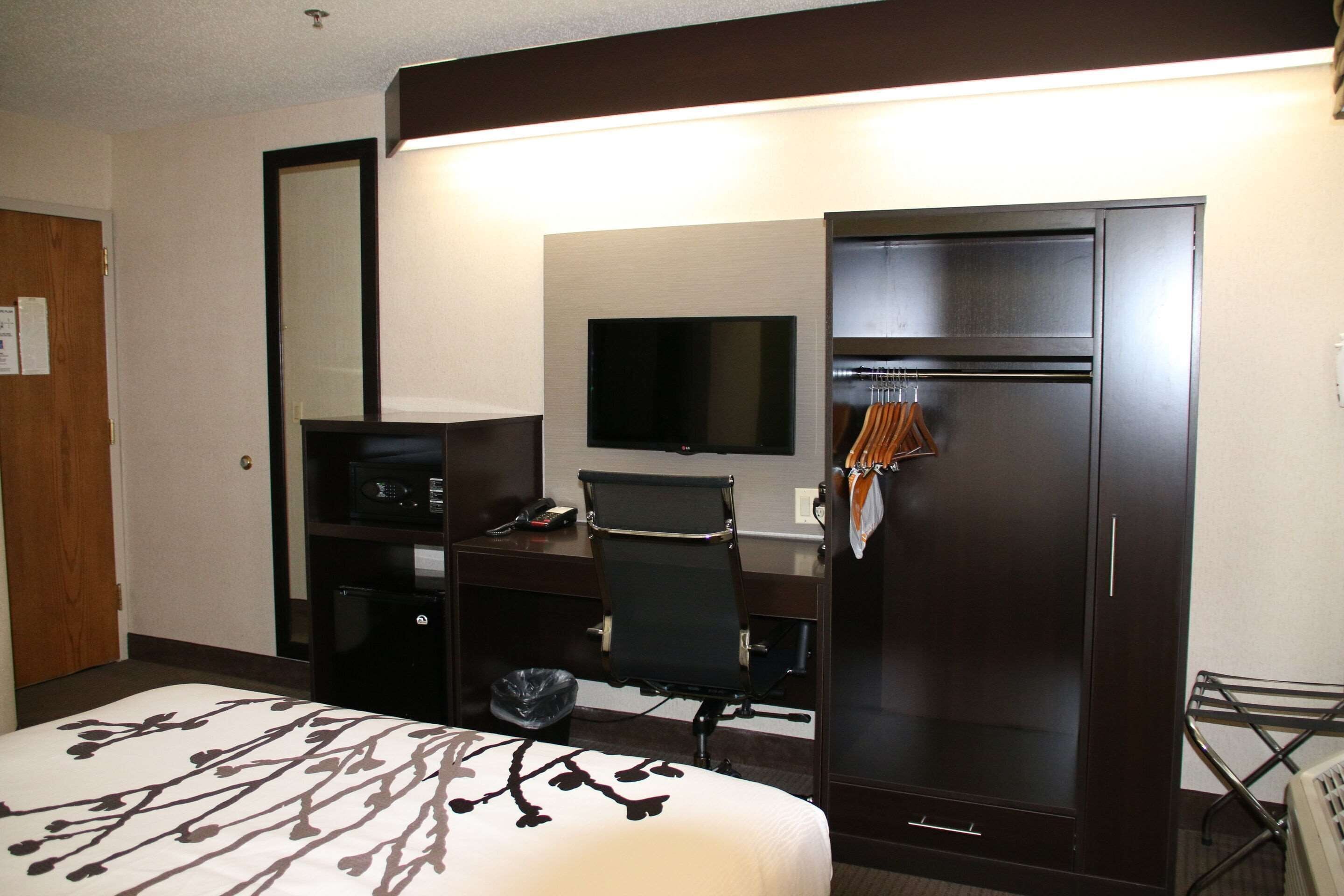 Une chambre d’hôtel équipée d’un lit, d’un bureau, d’une chaise, d’une télévision, d’une armoire et d’une petite poubelle.