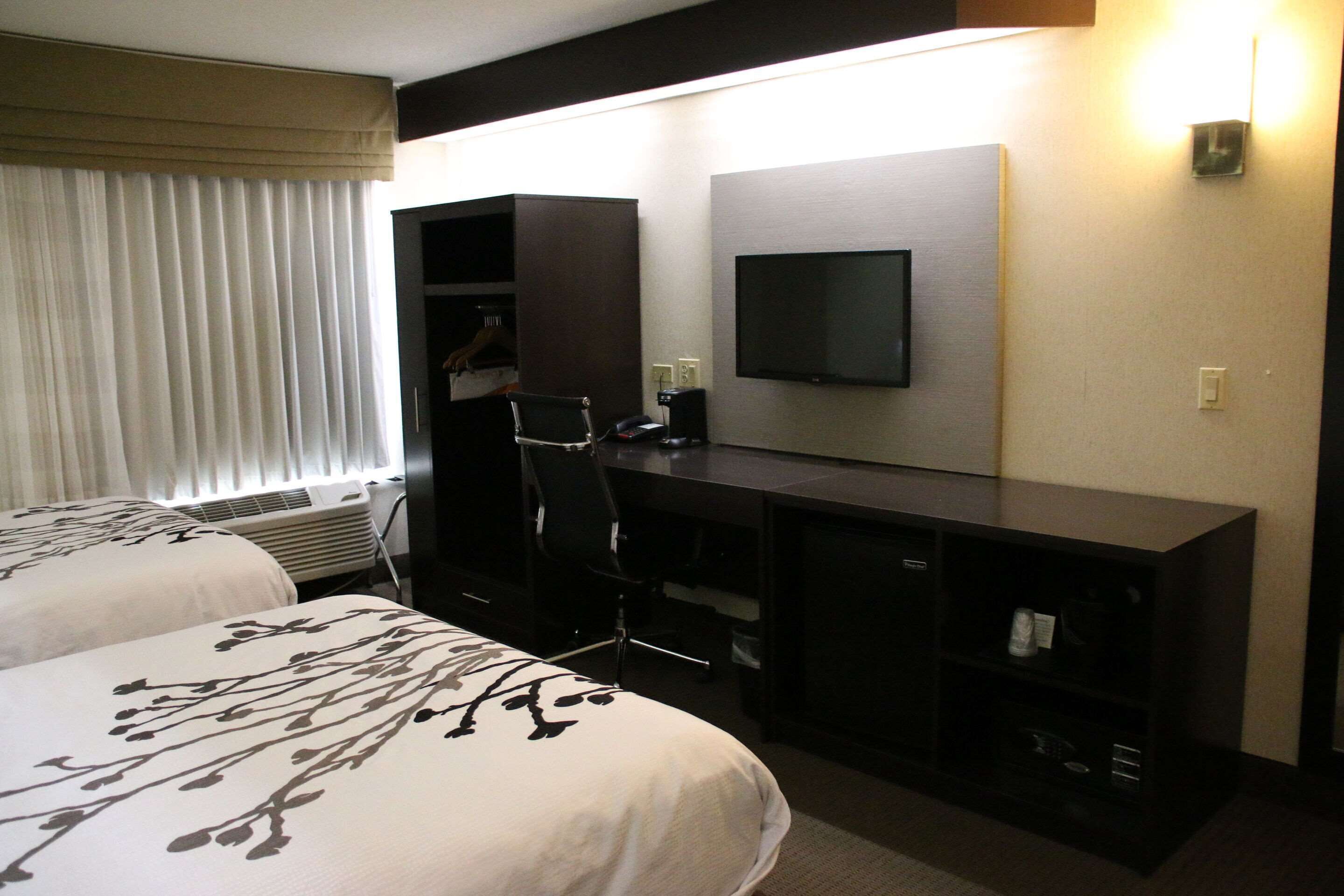 Une chambre d’hôtel avec deux lits, un bureau, une chaise, une télévision et une armoire.